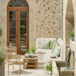 Rincón del patio con banco corrido, cojines verdes, sillas de mimbre, puerta arqueada y escultura