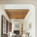 Salón con vigas de madera, arco blanco, chimenea de piedra, butacas y sofá claro