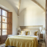 Dormitorio con techo abovedado, balconera con postigo de madera, cama de colcha amarilla y suelo hidráulico
