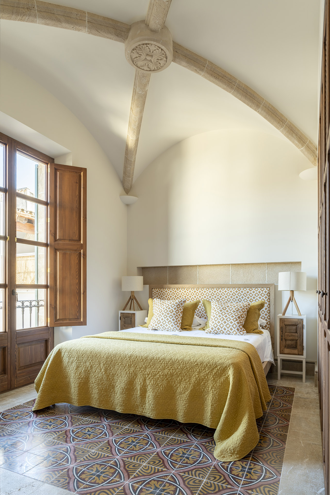 Dormitorio con techo abovedado, balconera con postigo de madera, cama de colcha amarilla y suelo hidráulico