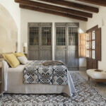 Dormitorio con pared de piedra, armarios de madera con celosía, colcha geométrica y suelo de baldosa decorativa