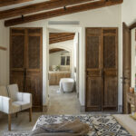 Dormitorio con puertas de celosía de madera y, al fondo, baño con bañera exenta bajo vigas