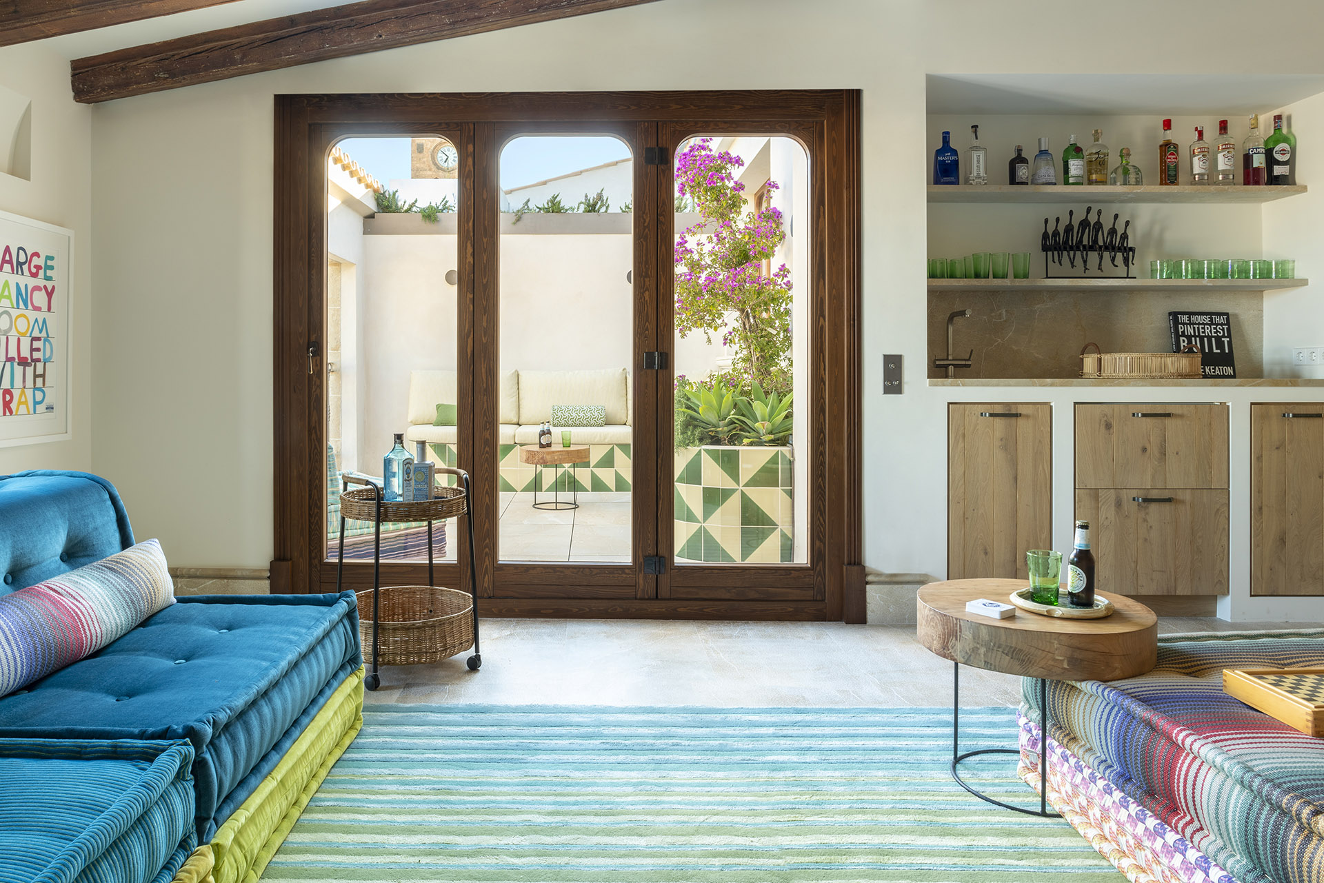 Sala con puertas acristaladas de madera hacia la terraza, sofá turquesa y estantes de bar