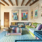 Sala de estar con sofás modulares multicolor, alfombra turquesa, rincón de bar y pared de piedra
