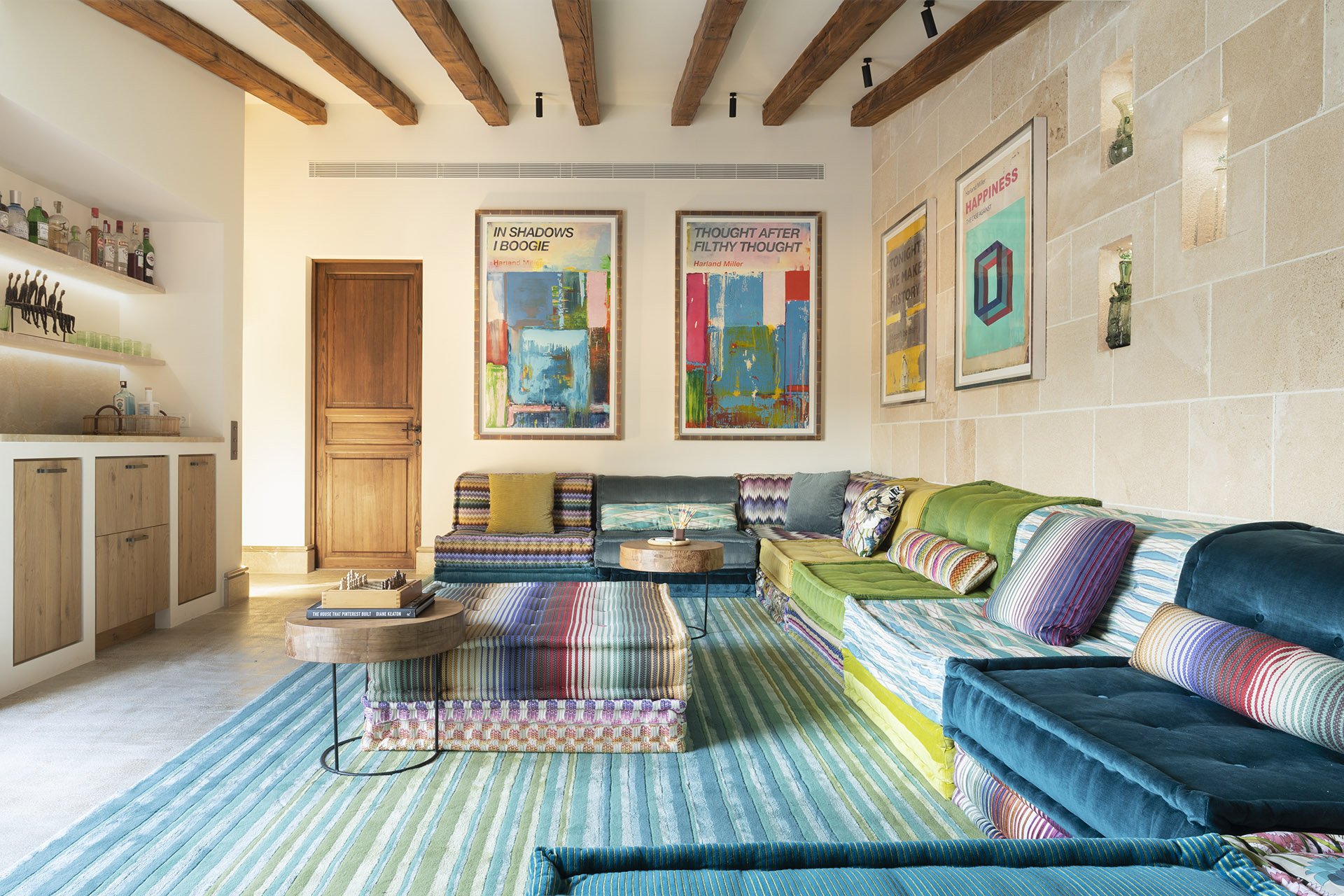 Sala de estar con sofás modulares multicolor, alfombra turquesa, rincón de bar y pared de piedra