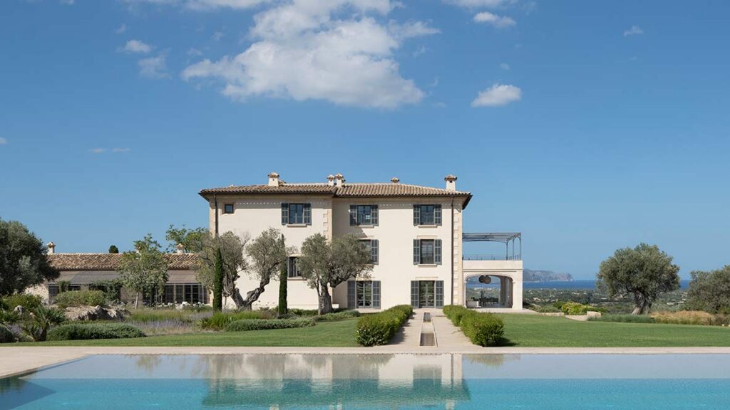 Fassade des Herrenhauses mit grauen Fensterläden, Olivenbäumen, Pool im Vordergrund und Meer im Hintergrund