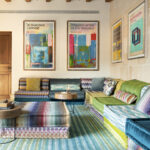 Sala de estar colorida con sofás modulares, alfombra de rayas turquesa, láminas enmarcadas y vigas de madera