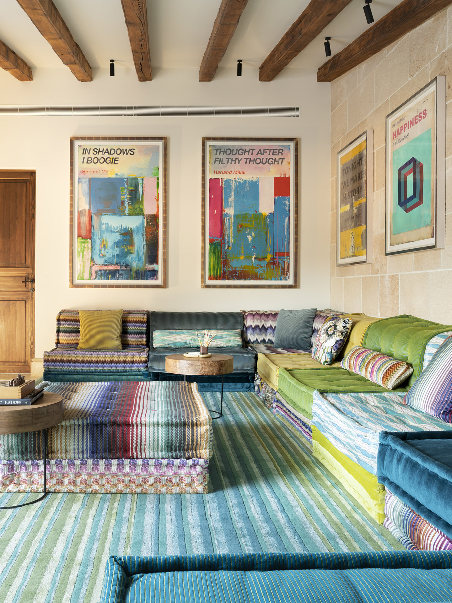 Sala de estar colorida con sofás modulares, alfombra de rayas turquesa, láminas enmarcadas y vigas de madera