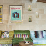 Detalle del sofá modular verde, amarillo y azul bajo pared de piedra con nichos y cuadro