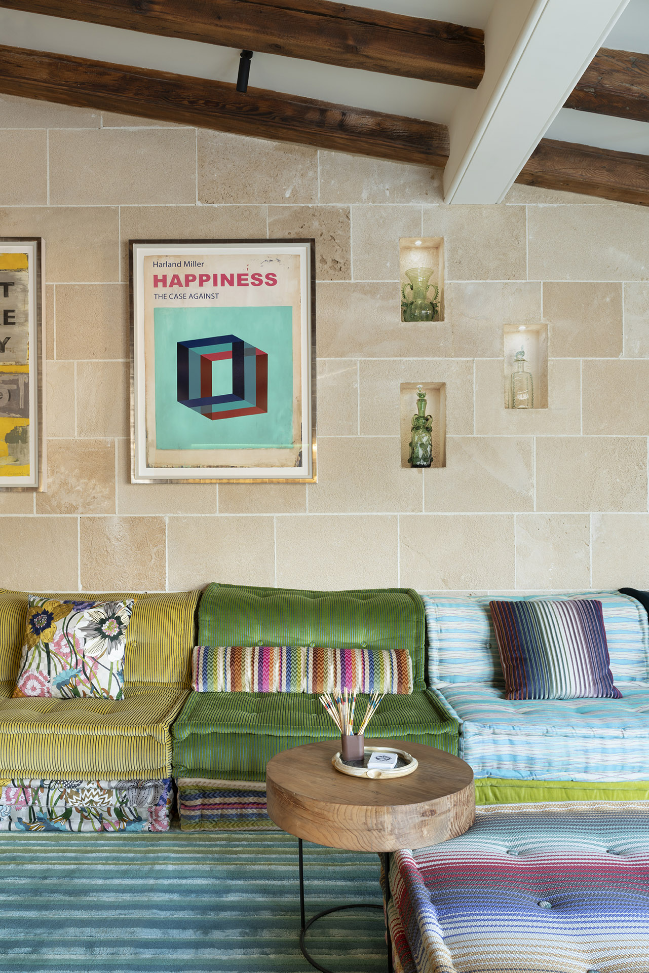 Detalle del sofá modular verde, amarillo y azul bajo pared de piedra con nichos y cuadro