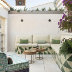 Terraza en altura con banco revestido de azulejos verdes, mesas de madera, buganvilla y torre con reloj