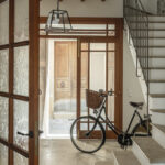 Acceso con puerta acristalada de madera, bicicleta antigua, lámpara colgante y escalera de peldaños de piedra