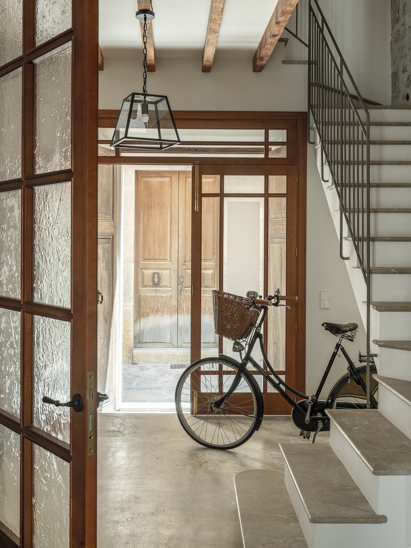Acceso con puerta acristalada de madera, bicicleta antigua, lámpara colgante y escalera de peldaños de piedra