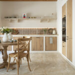 Cocina comedor con muebles de madera, salpicadero de azulejos, estante abierto, mesa redonda y suelo de piedra