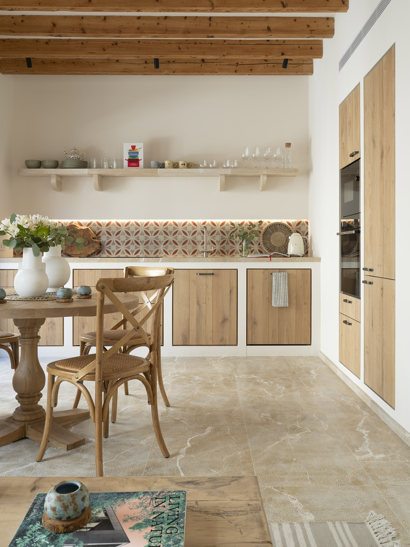 Cocina comedor con muebles de madera, salpicadero de azulejos, estante abierto, mesa redonda y suelo de piedra