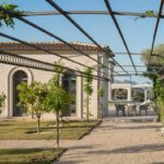 Große Bogenfenster des Pavillons zwischen Zitrusbäumen, eingerahmt von Metallpergola und Kletterpflanzen