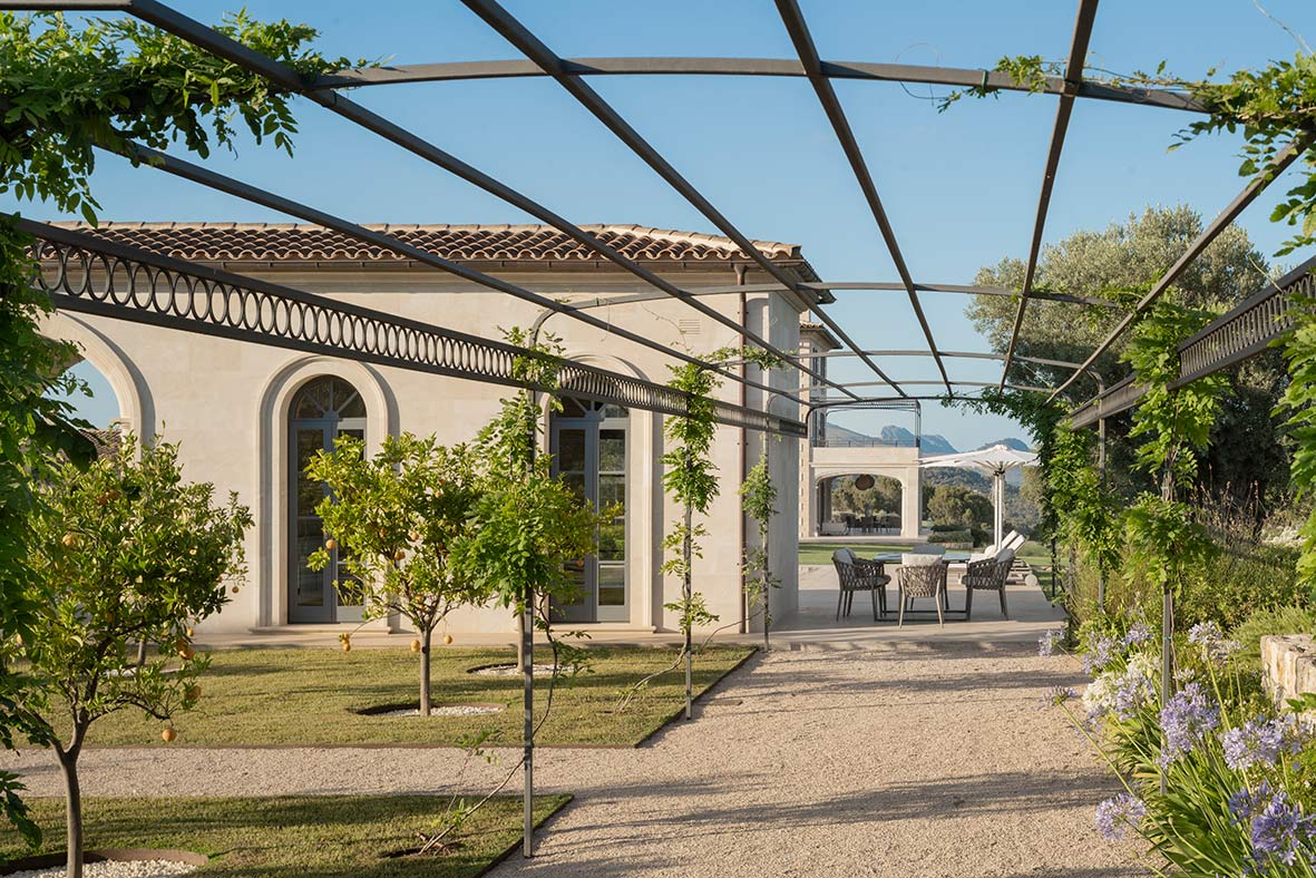 Große Bogenfenster des Pavillons zwischen Zitrusbäumen, eingerahmt von Metallpergola und Kletterpflanzen
