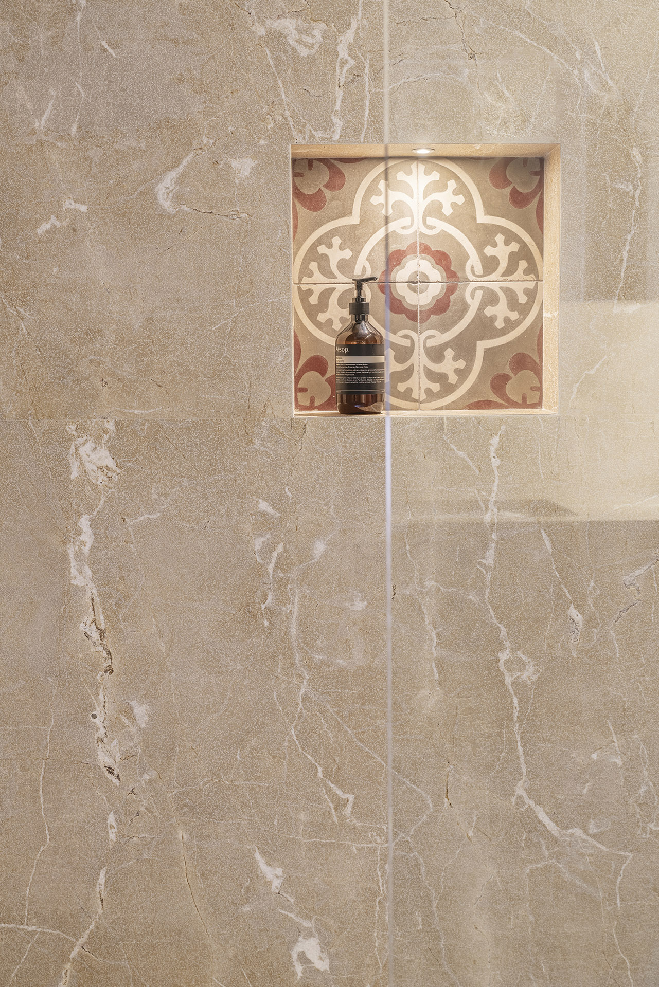 Detalle de ducha con pared de mármol beige y hornacina revestida de baldosa hidráulica