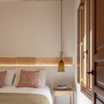 Dormitorio con franja de piedra iluminada, lámpara colgante de campana, cojines rojos y ventana de madera
