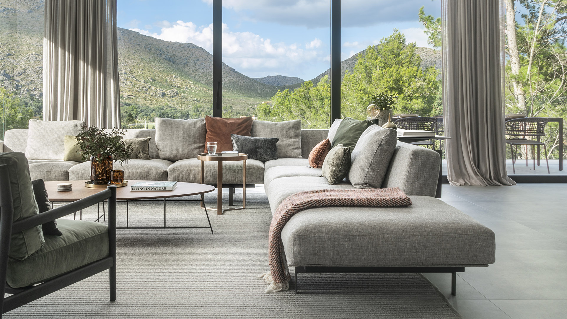 Graues Modulsofa mit terrakottafarbenen und grünen Kissen vor großen Fenstern mit Blick auf die Berge