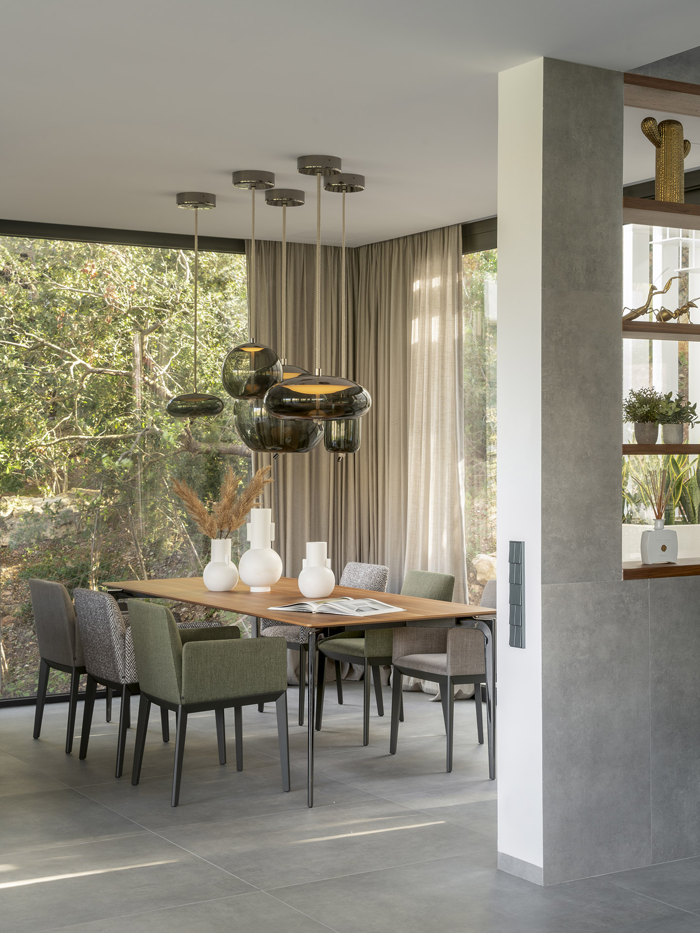Essbereich mit Holztisch, grün und grau gepolsterten Stühlen und Hängeleuchten aus Rauchglas