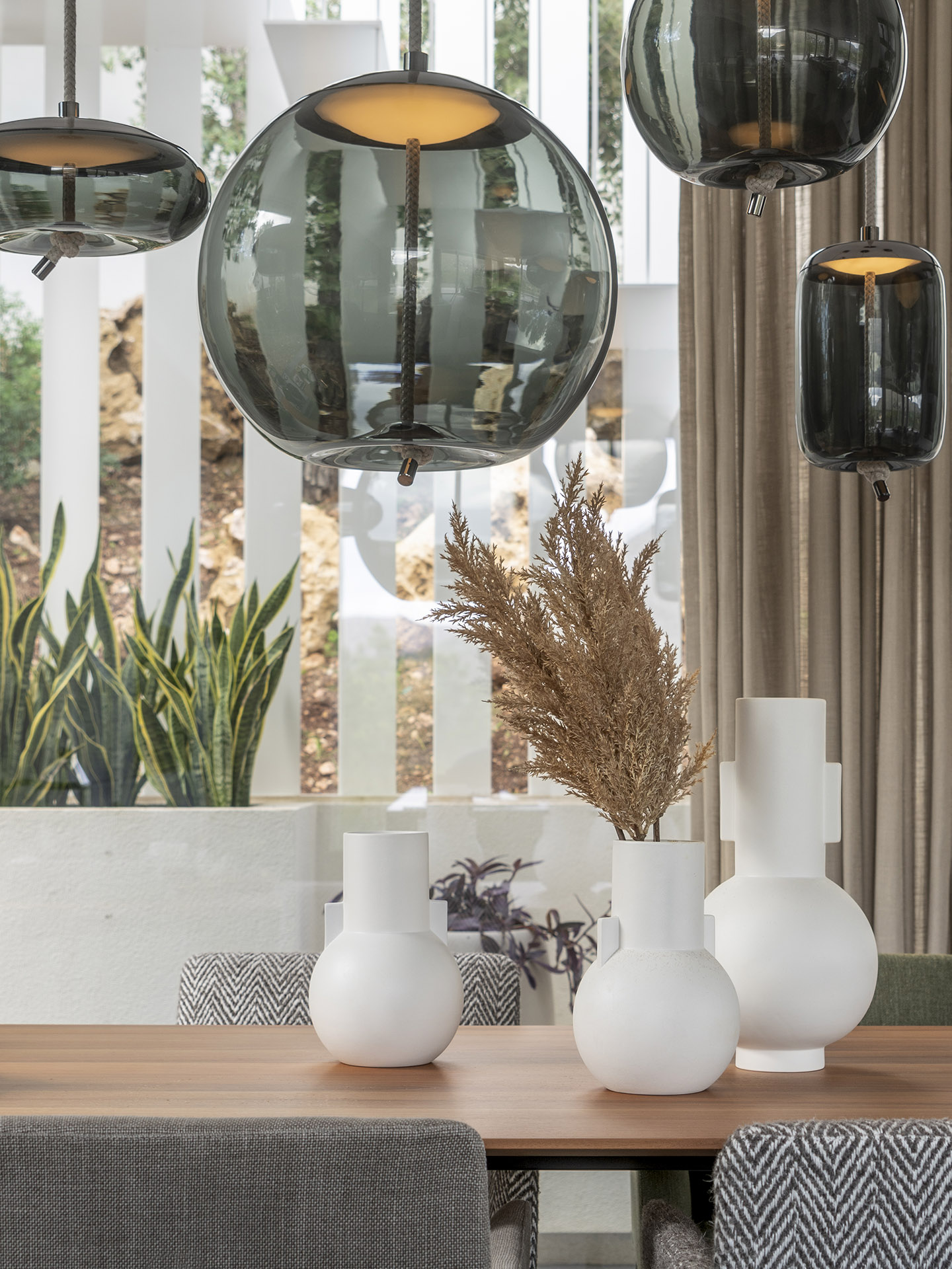 Detailansicht von Hängeleuchten aus Rauchglas über weißen Vasen und Trockenblumen auf dem Tisch