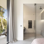 Schlafzimmer mit Ensuite-Bad, Glasdusche und Terrasse mit Sessel zwischen Kiefern