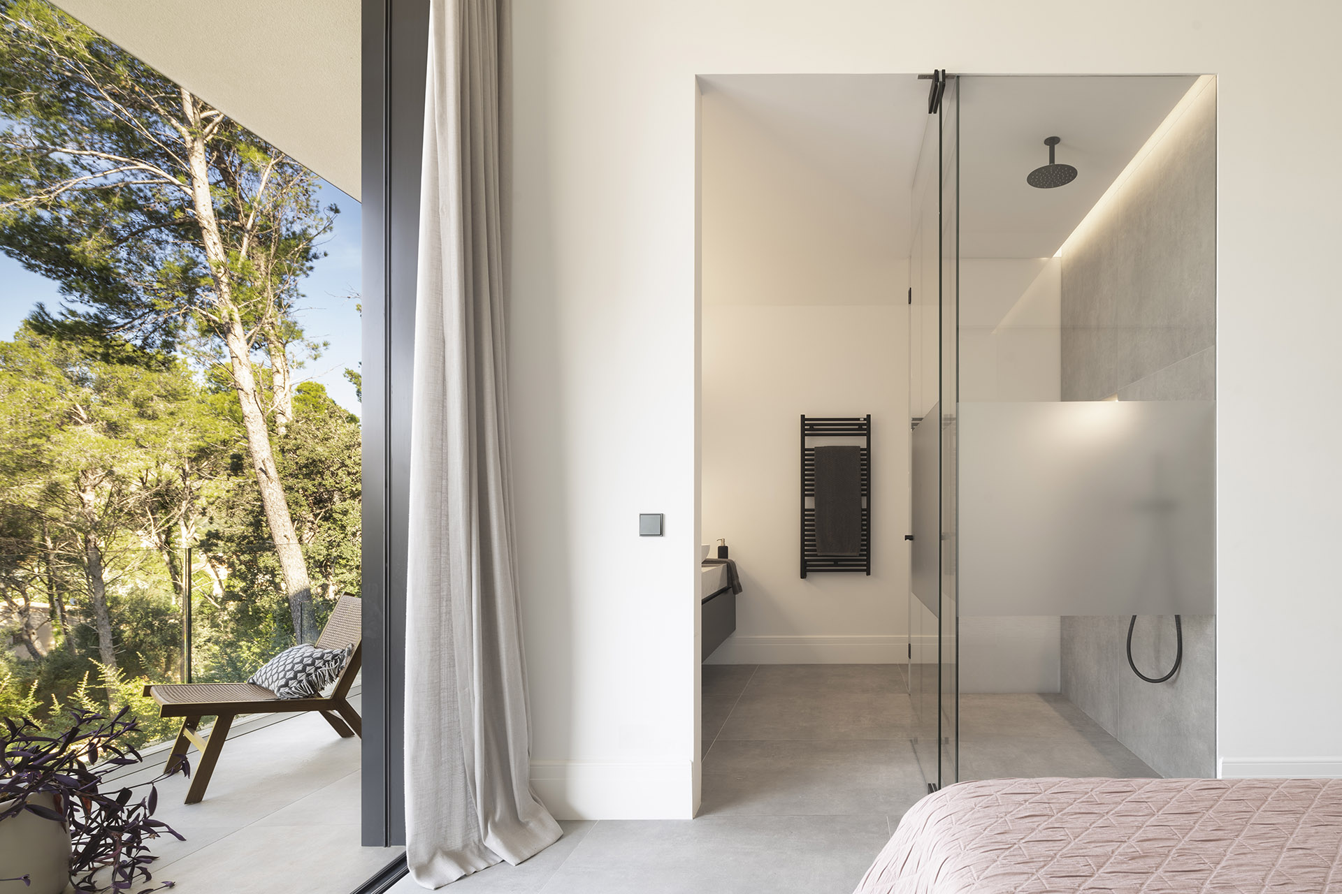 Schlafzimmer mit Ensuite-Bad, Glasdusche und Terrasse mit Sessel zwischen Kiefern