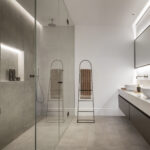 Badezimmer mit Glasdusche, Wand aus grauem Feinsteinzeug, weißer geäderter Arbeitsplatte und zwei Waschbecken