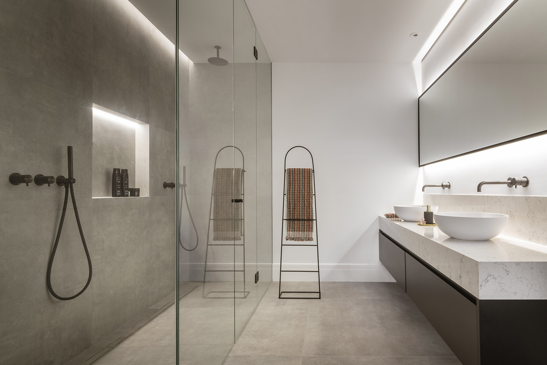 Badezimmer mit Glasdusche, Wand aus grauem Feinsteinzeug, weißer geäderter Arbeitsplatte und zwei Waschbecken