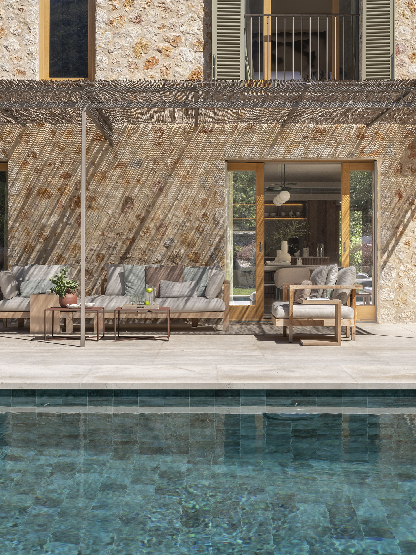 Terrasse am Swimmingpool mit Holzsofas, Pergola aus Schilfrohr und Steinfassade im Hintergrund