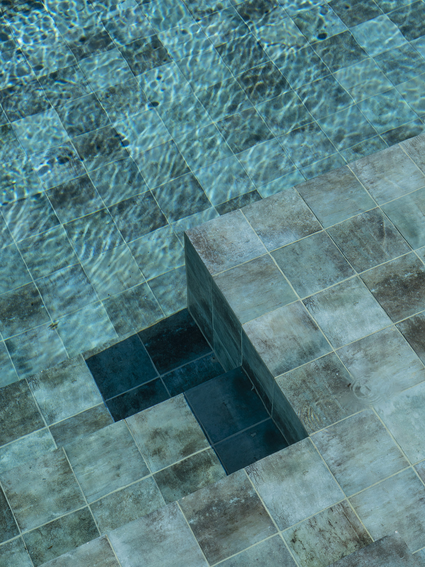 Detailansicht der Stufe des Swimmingpools mit blaugrüner Fliese und Spiegelungen im Wasser