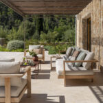 Terrasse mit Pergola aus Schilfrohr, Holzsofas und Holzsesseln, hellen Kissen und Steinwand