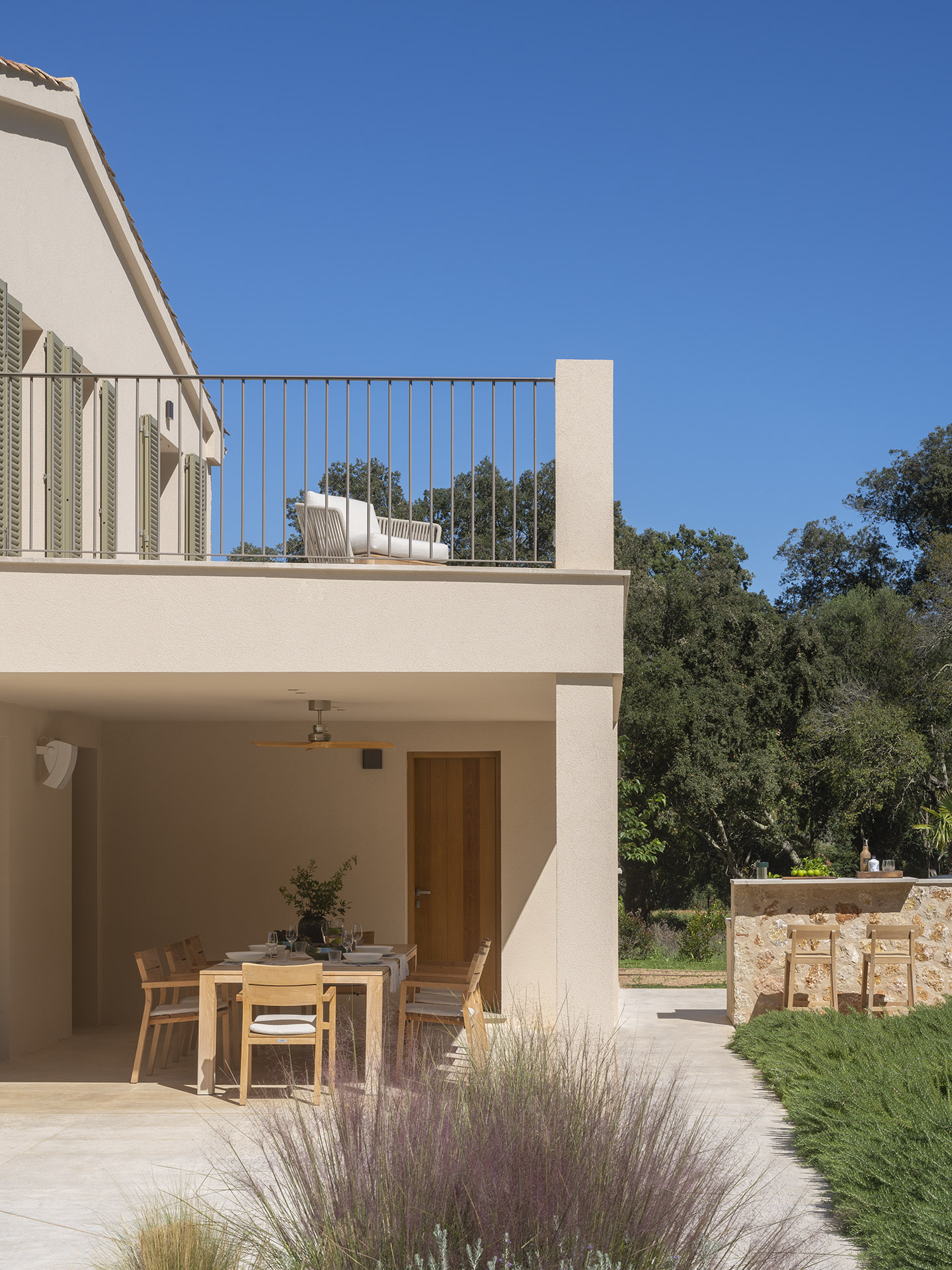 Veranda mit hölzernem Essbereich im Freien unter dem Balkon, Holztür und Steintheke mit Barhockern