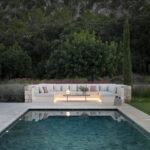 Chill-out-Bereich am Swimmingpool mit beleuchtetem gemauertem Sofa in der Abenddämmerung und bewaldetem Hang im Hintergrund
