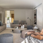 Wohnzimmer mit beigefarbenen Sofas, Ledersessel in natürlichem Lederton, grauen Poufs und Kamin rechts
