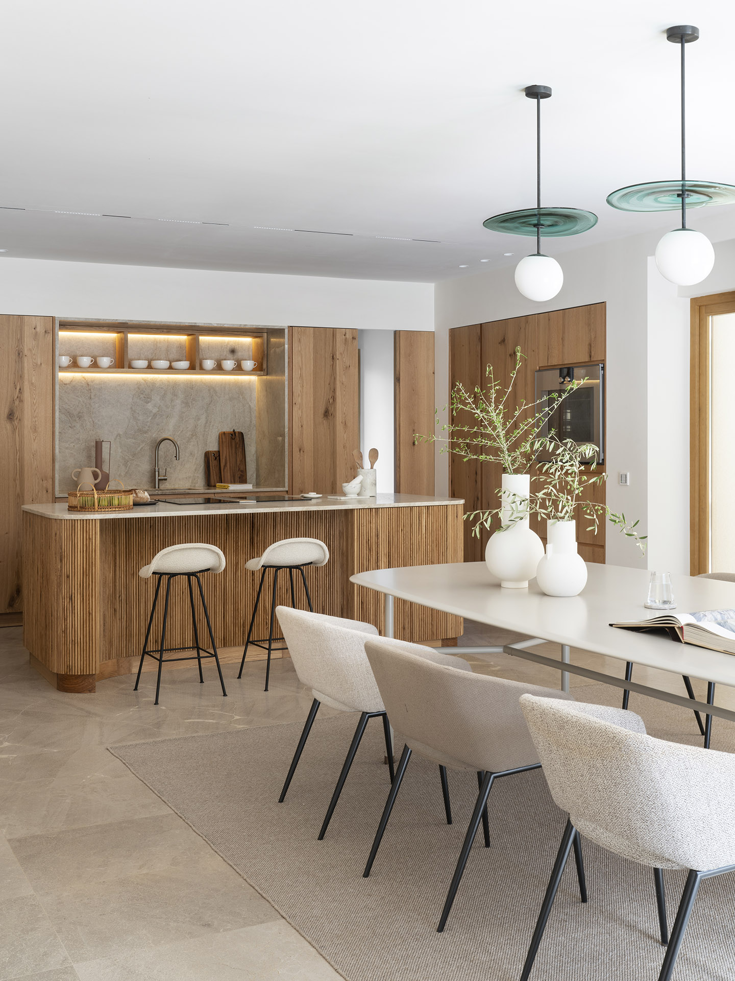 Offene Küche zum Essbereich mit Insel aus Holzlamellen, Barhockern, hellem Tisch und gepolsterten Stühlen