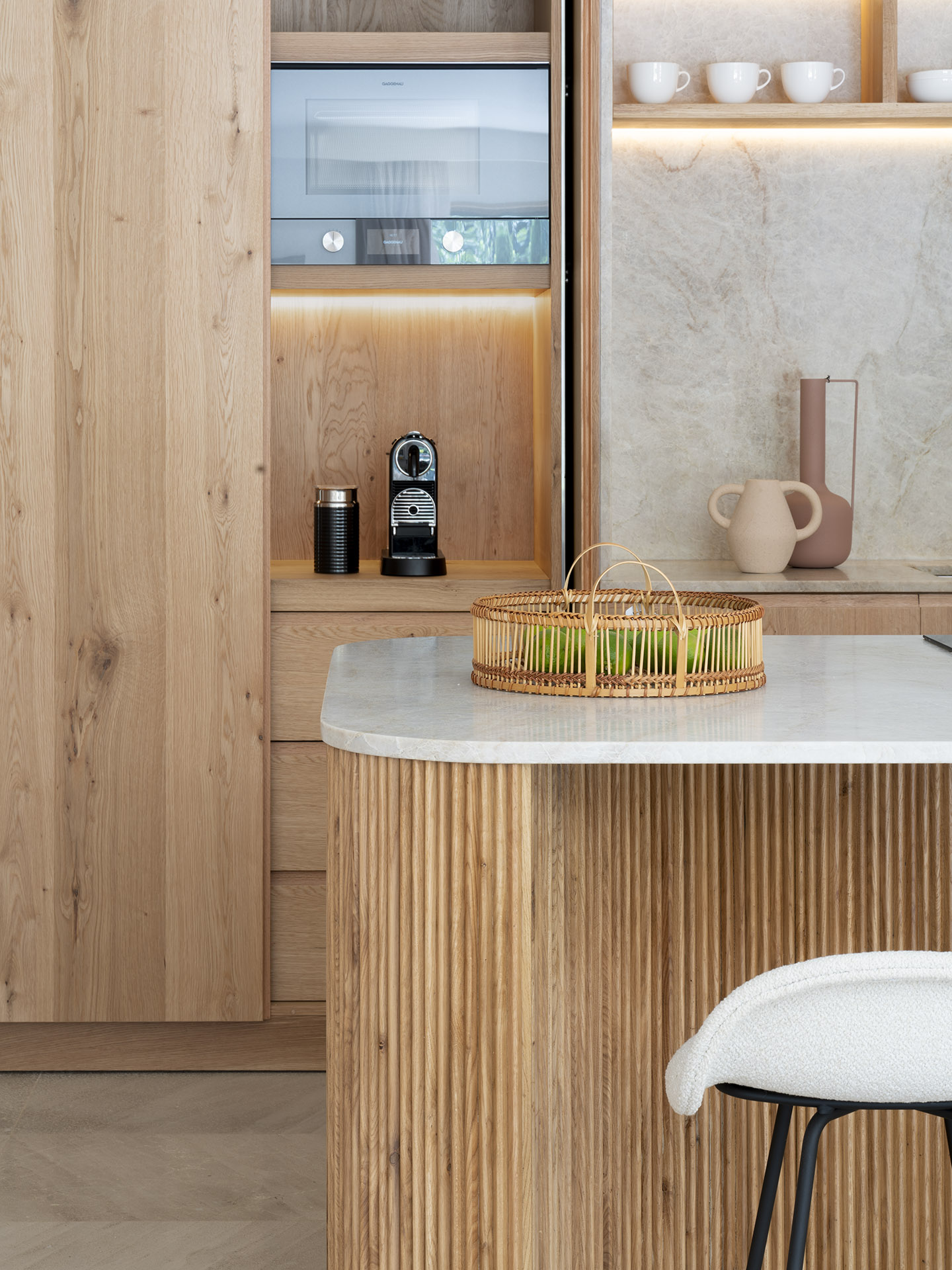 Detailansicht von Holzschränken mit integrierten Elektrogeräten und Kaffeemaschine neben der geriffelten Kücheninsel