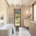 Badezimmer mit weißer freistehender Badewanne, Holztür zum Garten, wandhängendem Holzwaschtisch und Steinboden