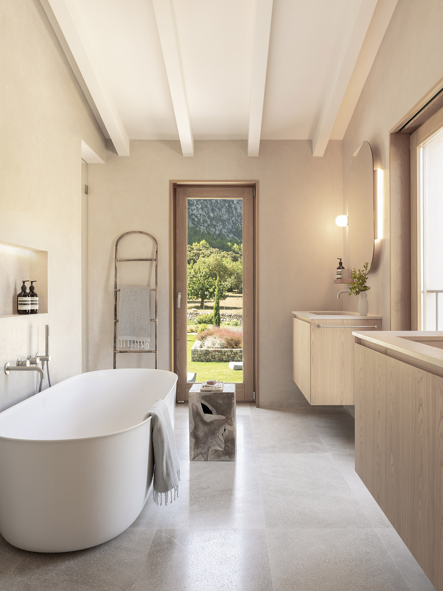 Badezimmer mit weißer freistehender Badewanne, Holztür zum Garten, wandhängendem Holzwaschtisch und Steinboden