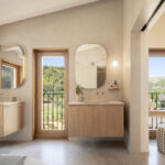 Badezimmer mit abgerundeten Spiegeln, wandhängenden Holzwaschtischen und Balkontür mit Blick auf die Bäume