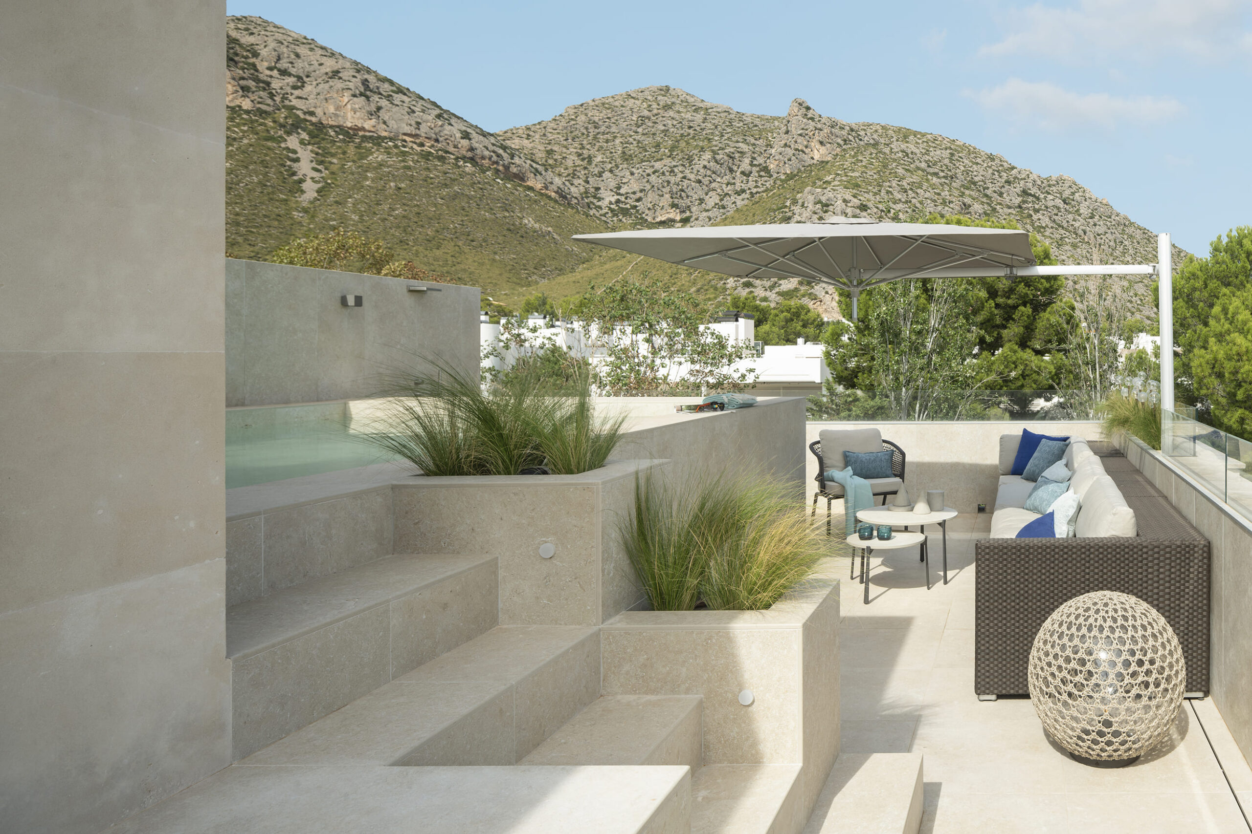Dachterrasse mit Steinstufen, Ziergräsern, Sofa im Freien, Sonnenschirm und Bergen im Hintergrund