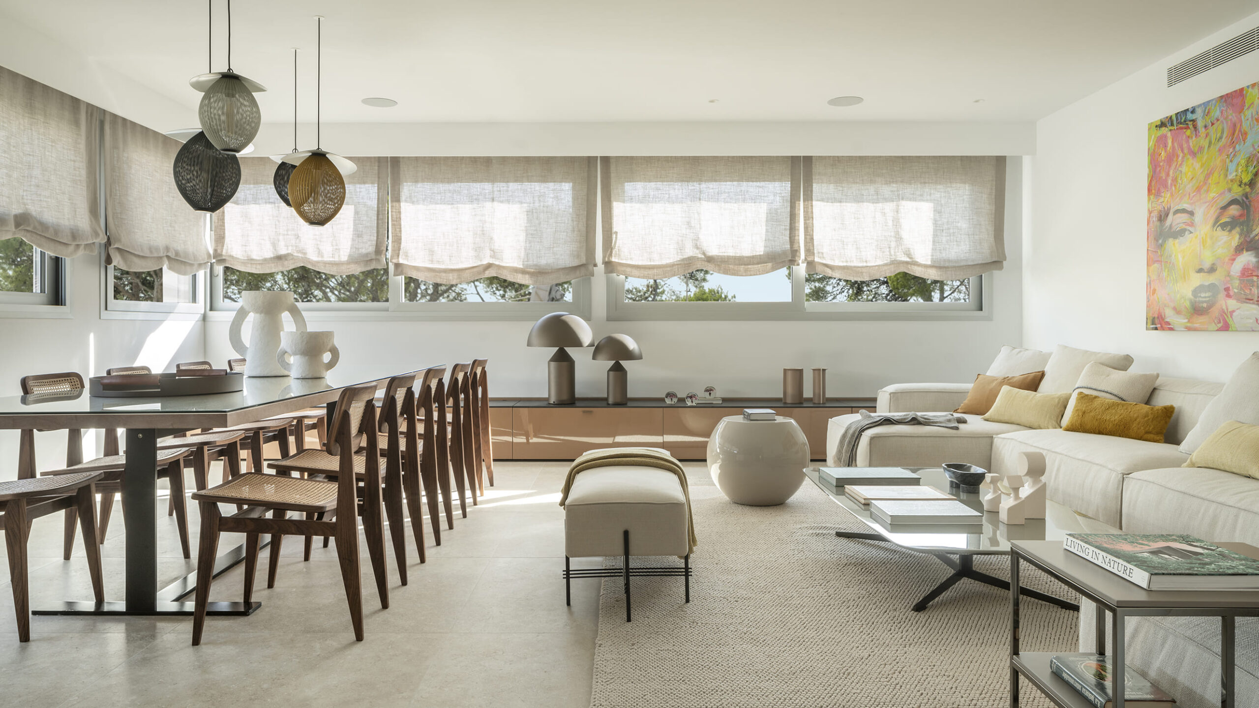 Heller Wohn- und Essbereich mit langem Tisch, Holzstühlen mit Rohrgeflecht, hellem Sofa und Leinenrollos