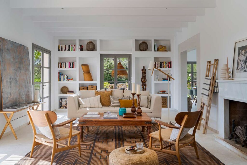 Bright living room with cream sofa, white built-in bookcase, wooden table, armchairs with woven seats and woven rug