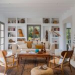 Bright living room with cream sofa, white built-in bookcase, wooden table, armchairs with woven seats and woven rug