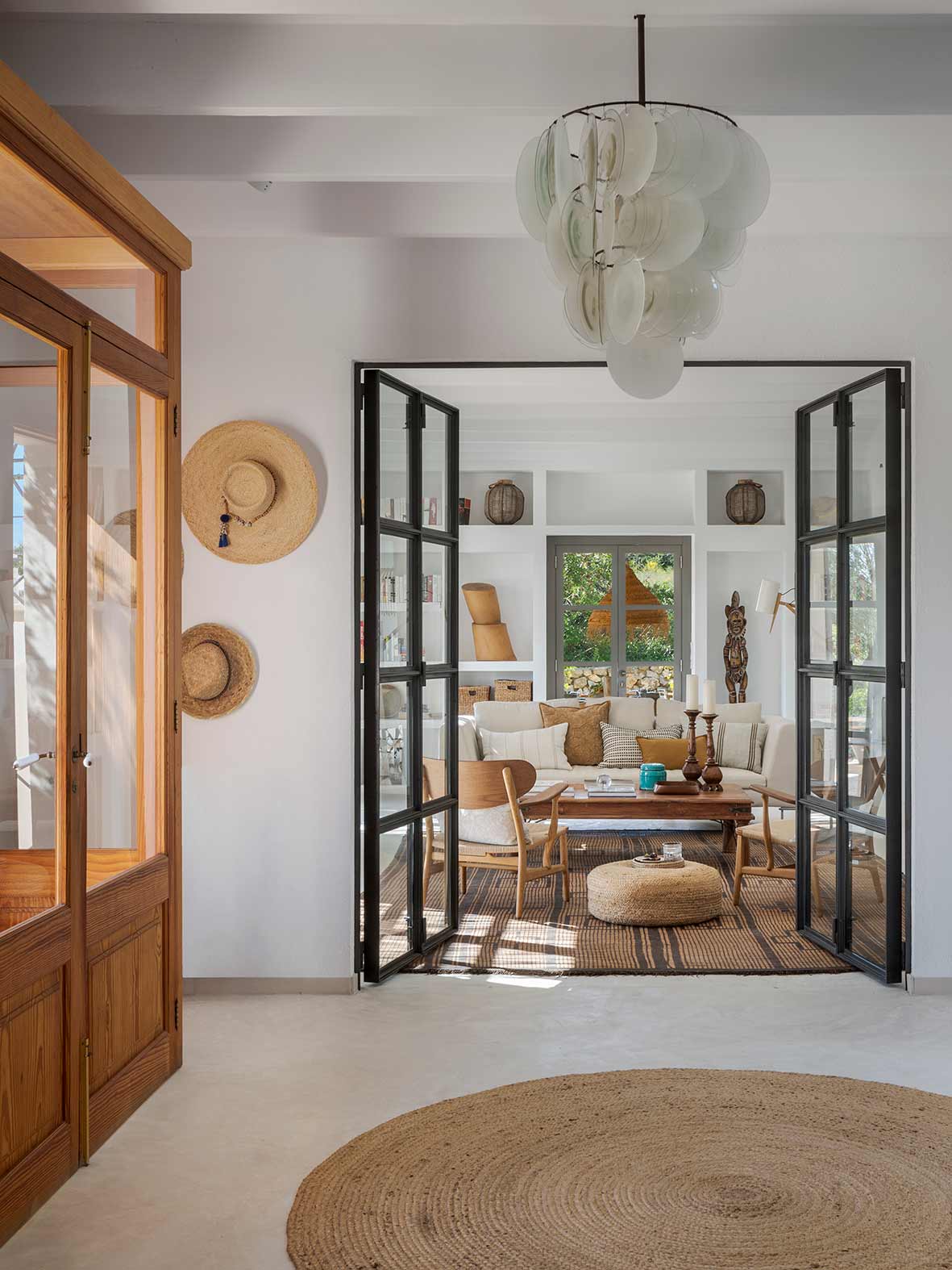 Glass and iron doors open to the living room, with translucent lamp, straw hats and jute rug