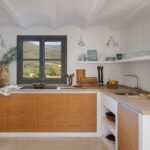 Kitchen with wooden cabinet fronts, beige stone worktop, vaulted ceiling and window with mountain views