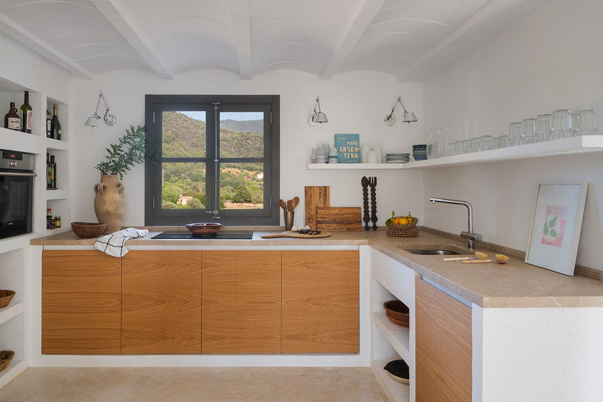 Kitchen with wooden cabinet fronts, beige stone worktop, vaulted ceiling and window with mountain views
