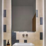 White basin on a countertop with mirror, wall-mounted taps and beige and grey-blue cement tiles