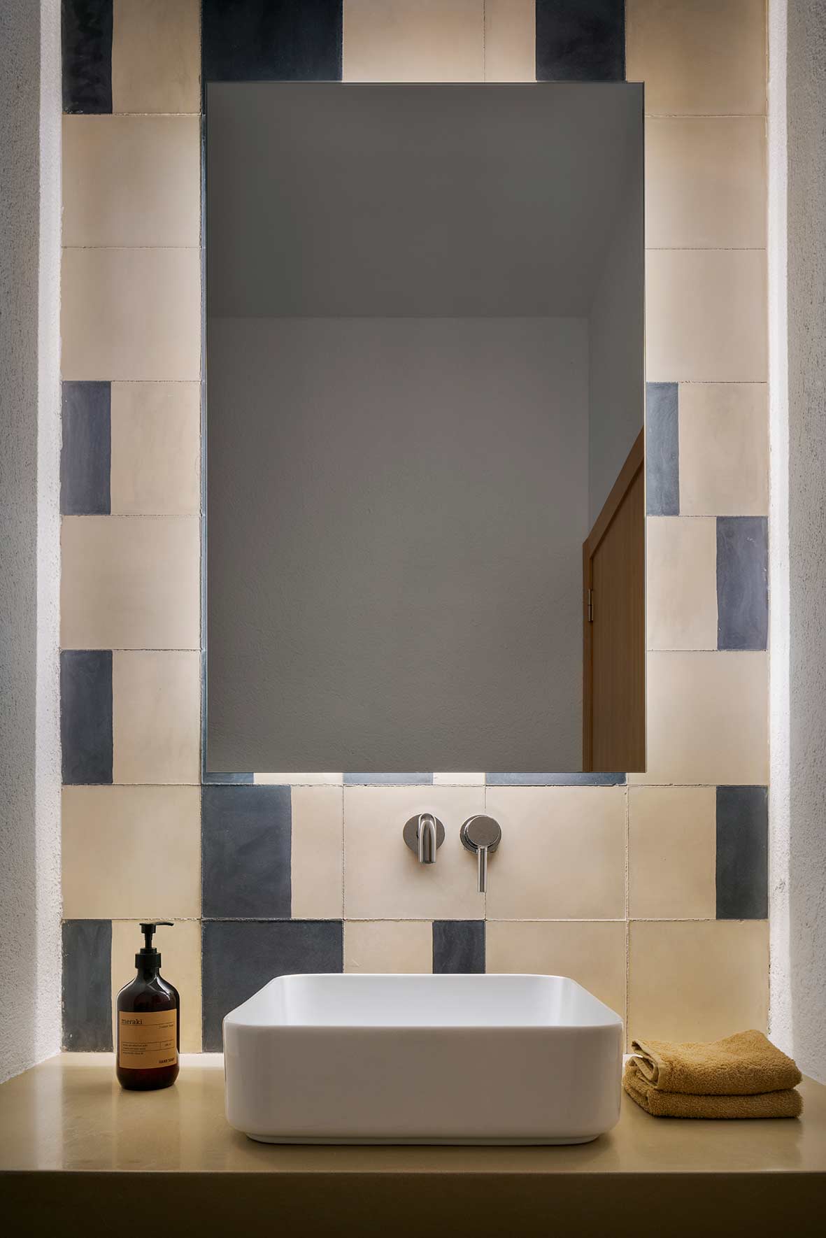 White basin on a countertop with mirror, wall-mounted taps and beige and grey-blue cement tiles